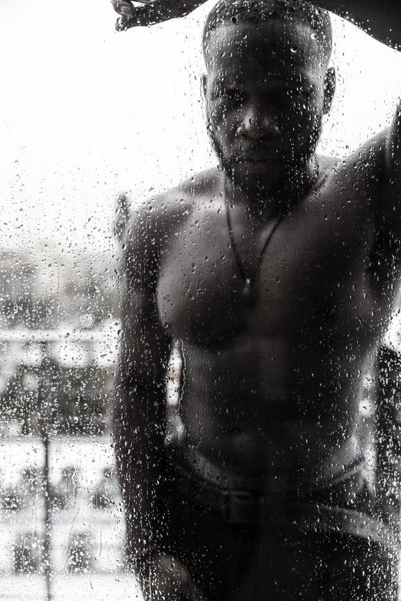 Artistic black and white photo of figure behind rain-streaked glass.