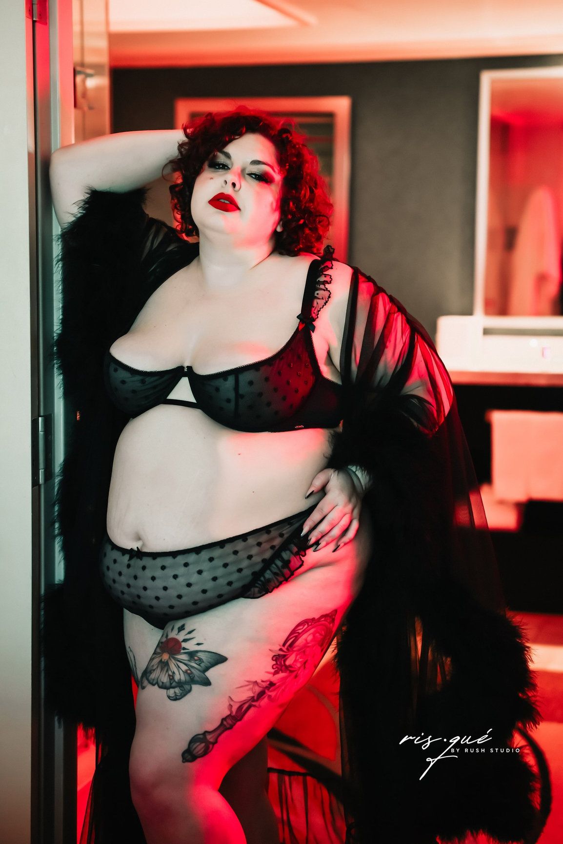 Boudoir photo with vintage-inspired lingerie and butterfly tattoo in dramatic red lighting.