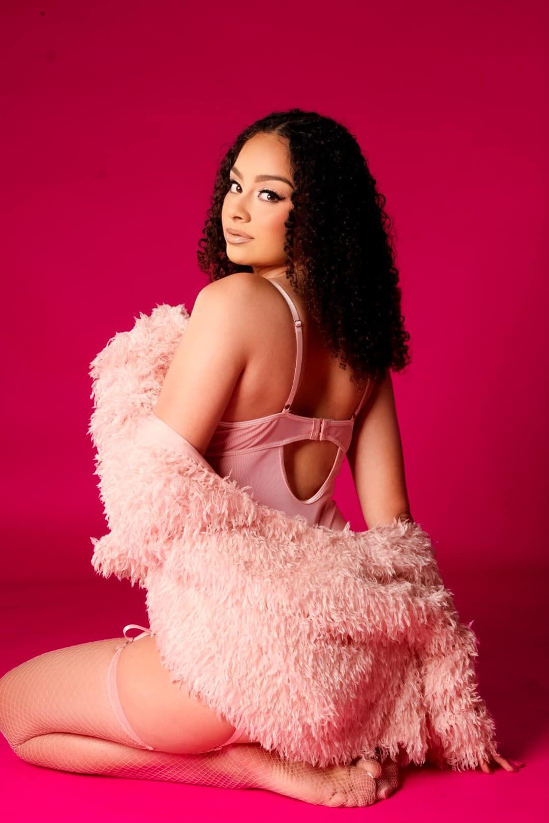 Artistic portrait featuring pink lingerie and fluffy robe against vibrant red background.