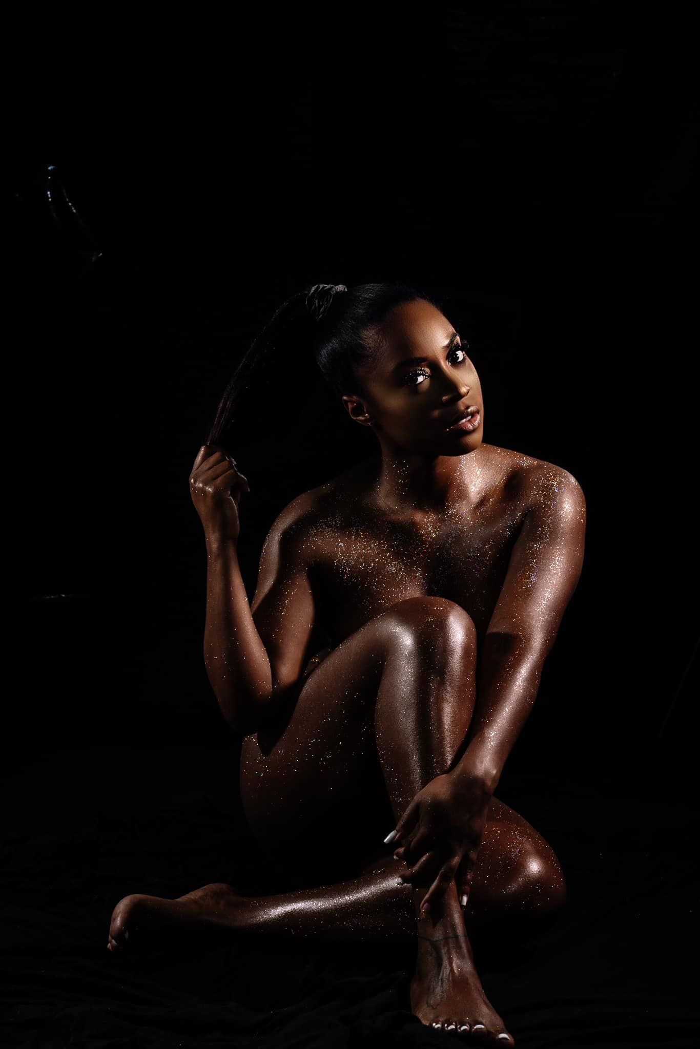 Artistic nude portrait with dramatic lighting against black background.