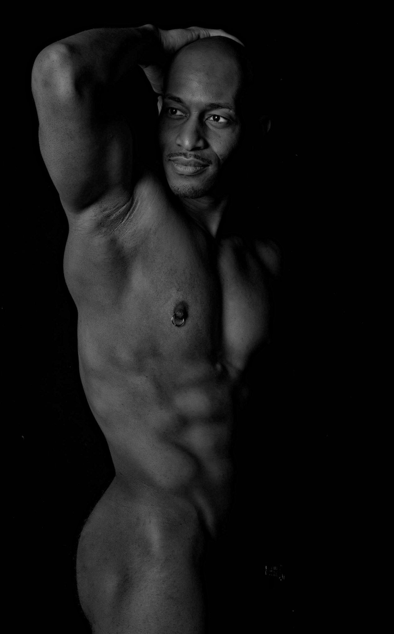 Artistic black and white portrait showcasing muscular physique against dark background.