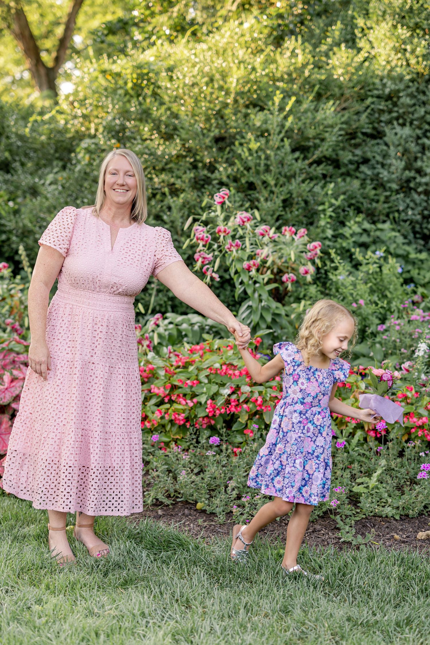 A joyful image of a mother and daughter surrounded by flowers and green trees.
