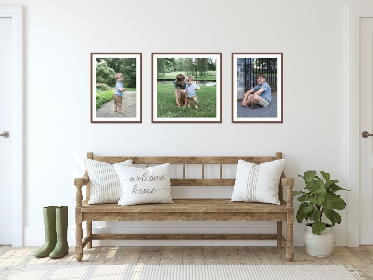 A rustic wooden bench with white pillows sits beneath three framed photos on a white wall, with green plants nearby.
