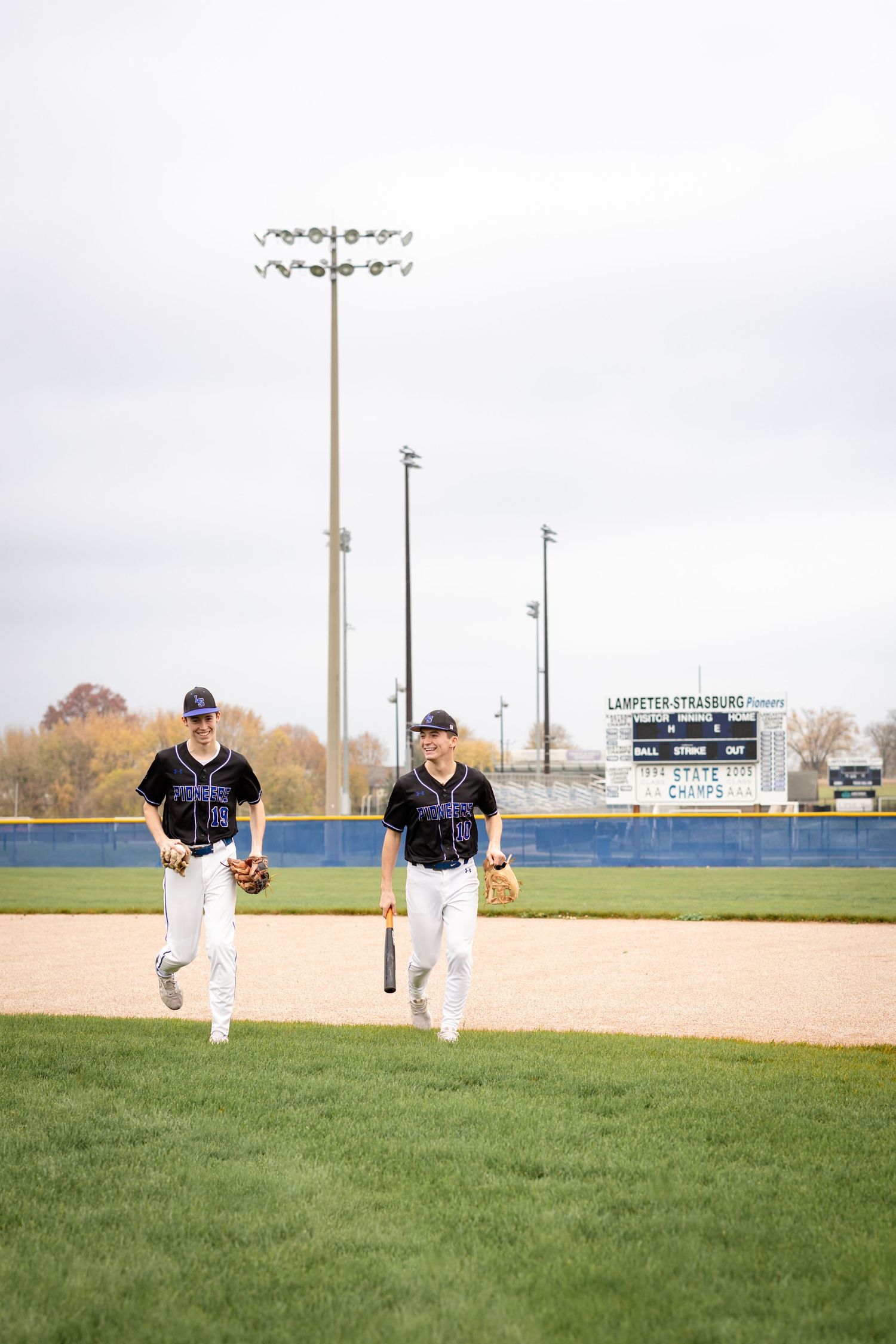 Two high school baseball players in navy uniforms running together for sports senior photos in Lancaster, PA.