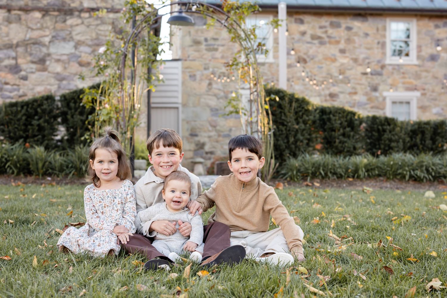 Children sitting together on grass near home in outdoor family photo session at Flourish Farmette