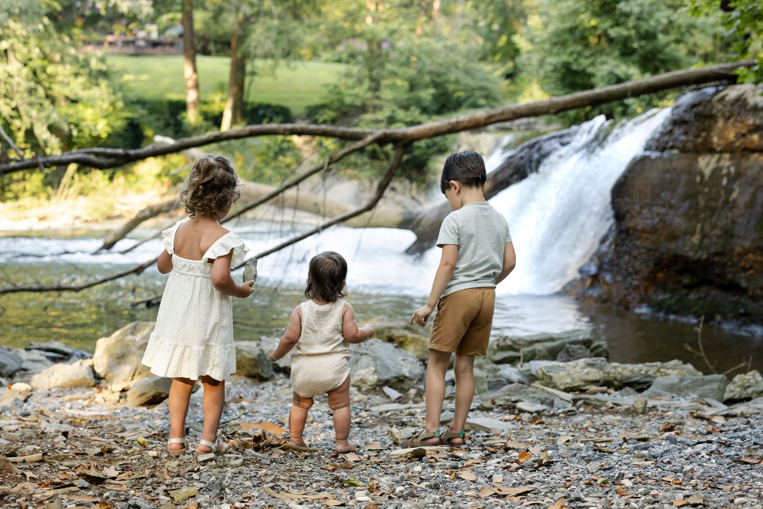 Children fish together on rocky riverbank while adults supervise during summer family photos in Millersville, PA.