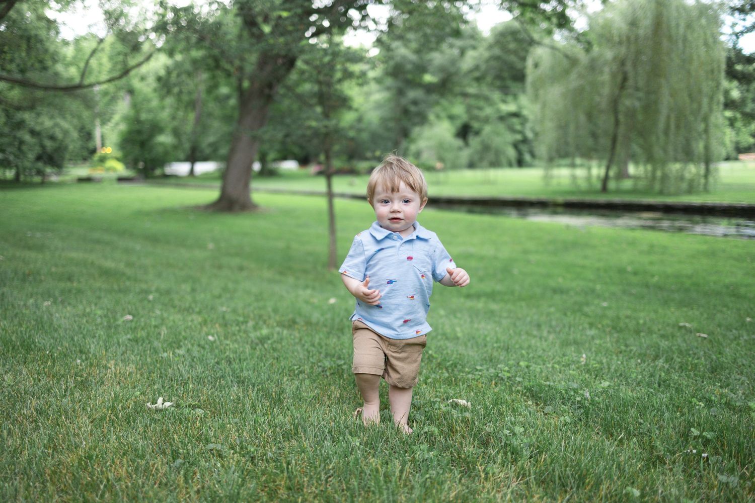 Small child in a blue shirt and khaki shorts runs playfully through lush green grass during Lancaster, PA family photography session.