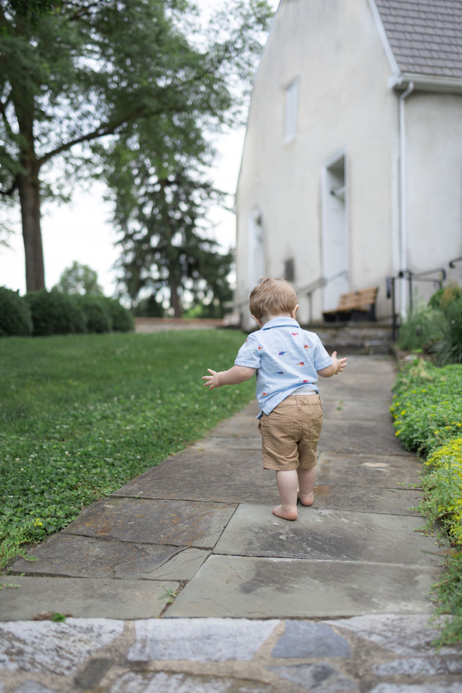 Small child walks up concrete steps while wearing tan shorts and blue shirt on a grassy slope during a Mount Joy, PA family photo session.