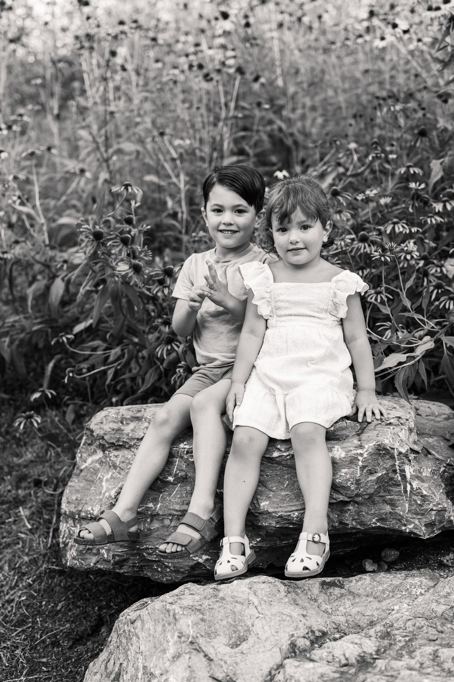 A black and white vintage photograph showing two children sitting together on a large rock by Lancaster, PA family photographer.