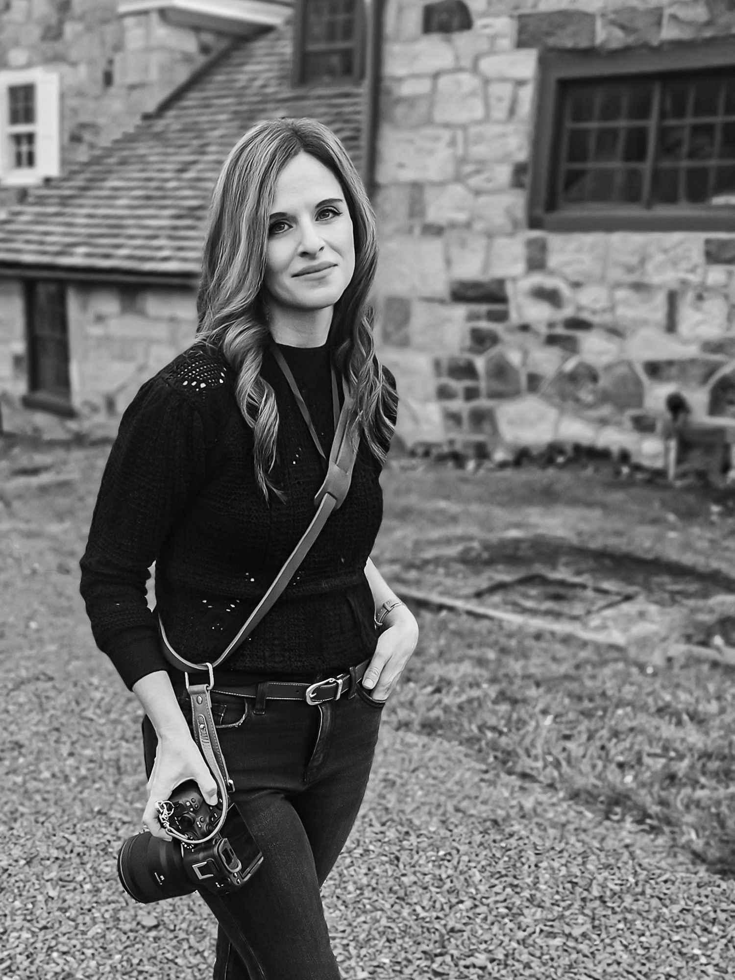Photographer with camera standing in front of rustic stone building.