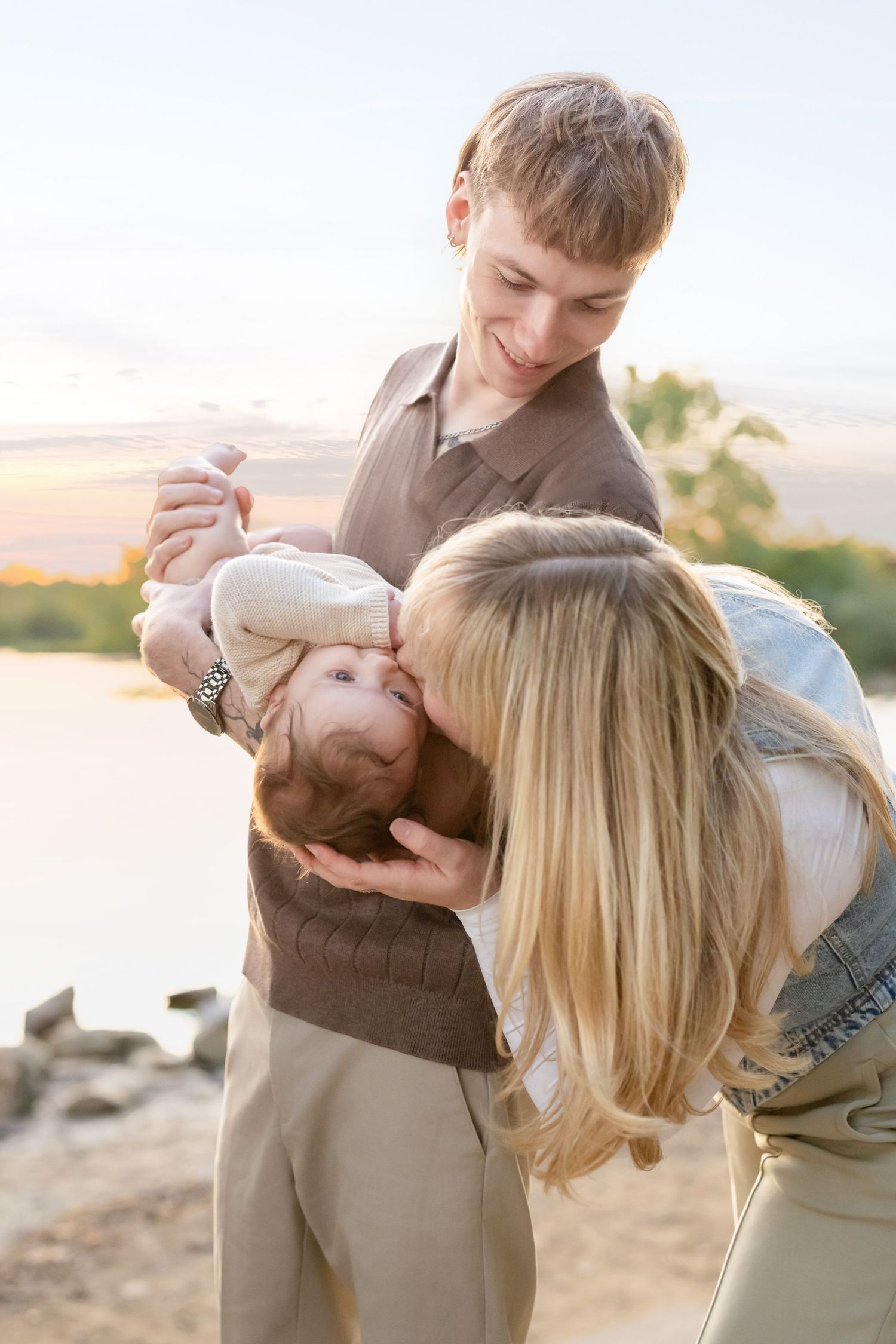 A couple in beige clothing embraces and dances together outdoors during sunset.