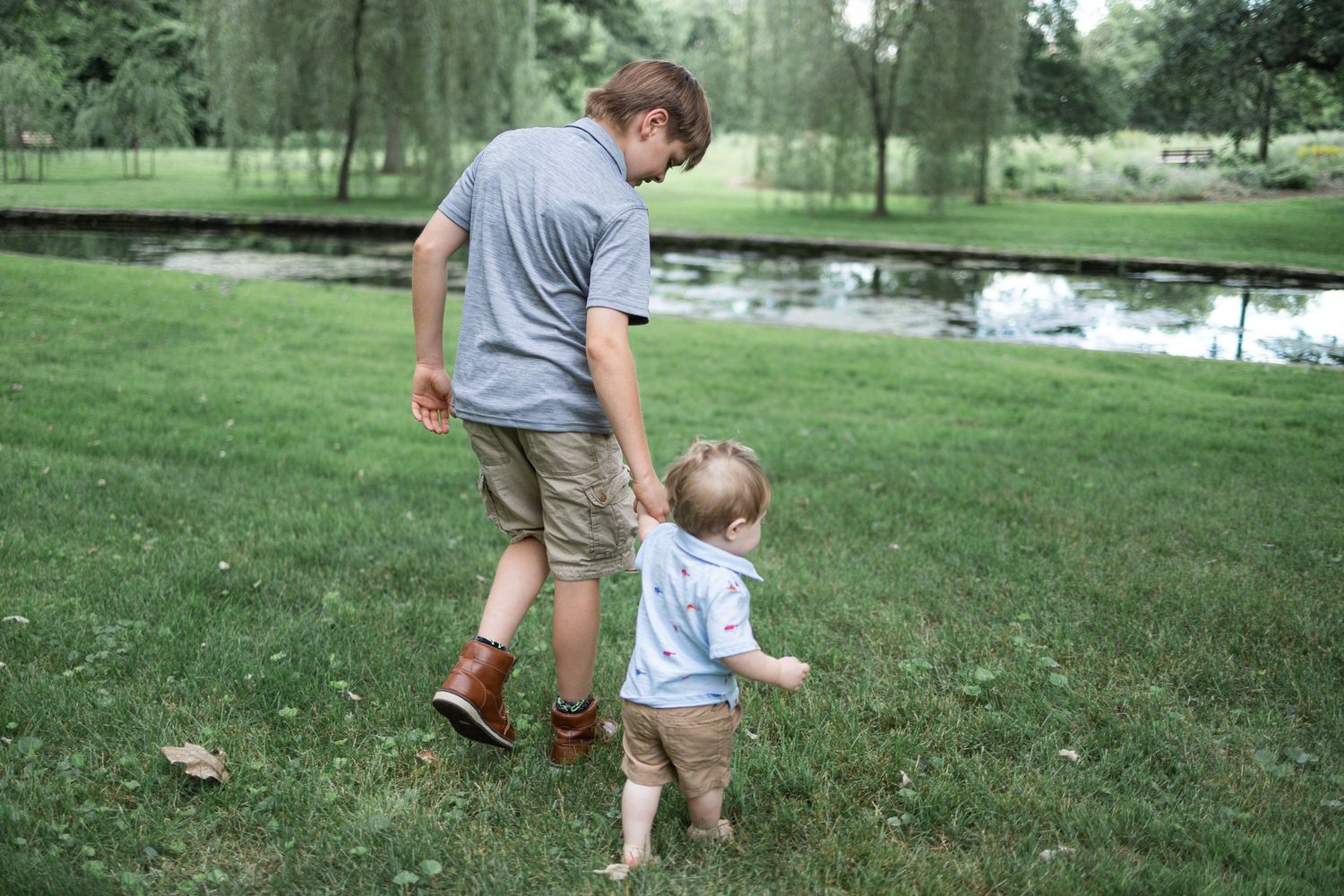 A teen and small child walk together on a lush green lawn at Donegal Presbyterian Church in Mount Joy, PA during family photos.