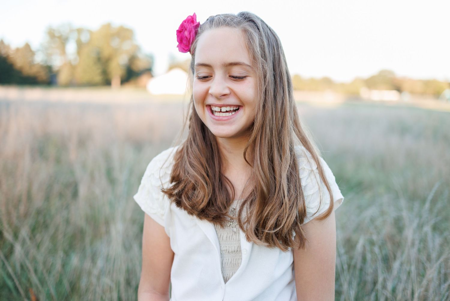 A girl is laughing in a beautiful grassy field at Overlook Park in Lancaster, PA during a family photography session.