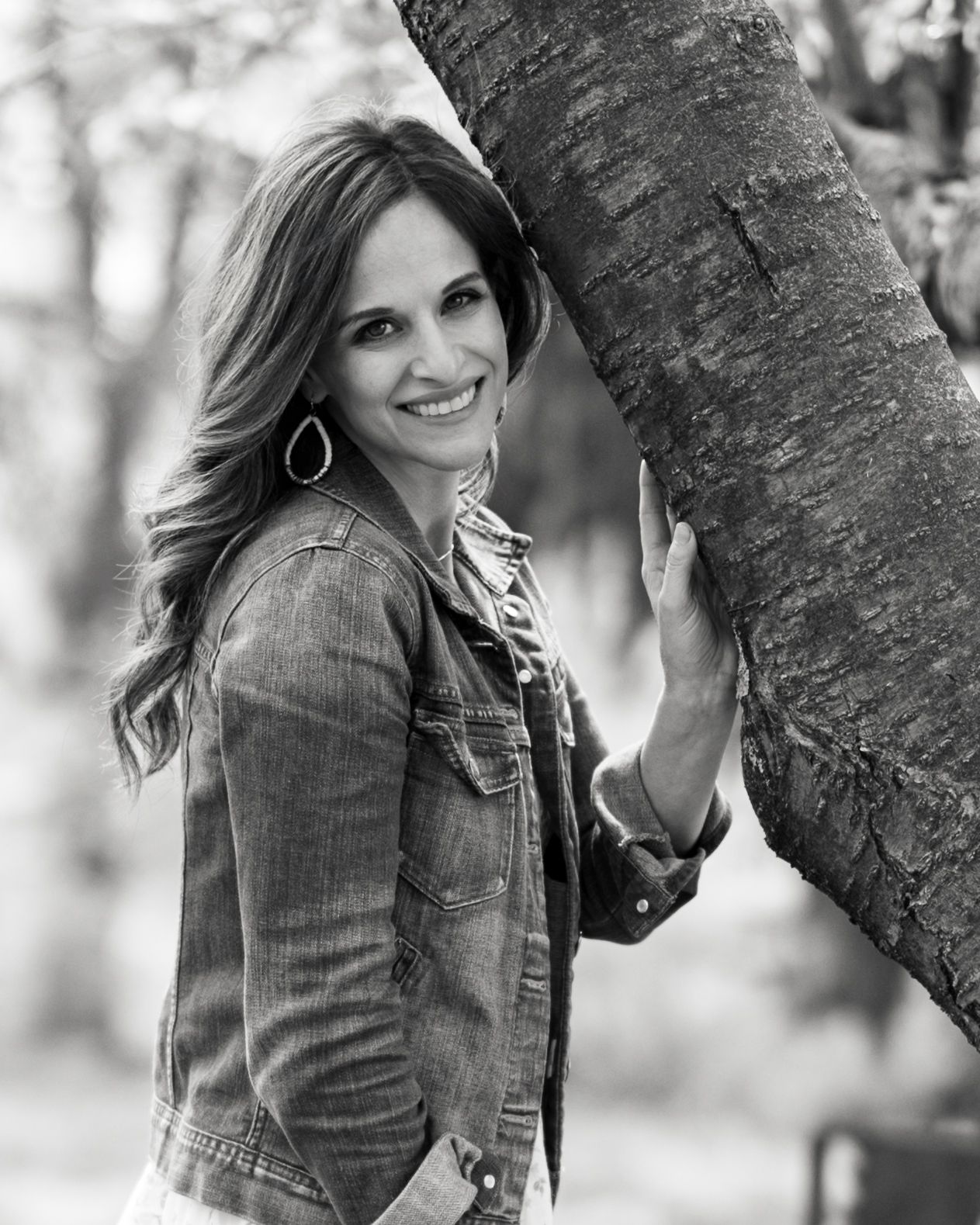 Megan Mariah, a luxury senior and family photographer in Lancaster, PA smiles by a large rustic tree in a park setting.
