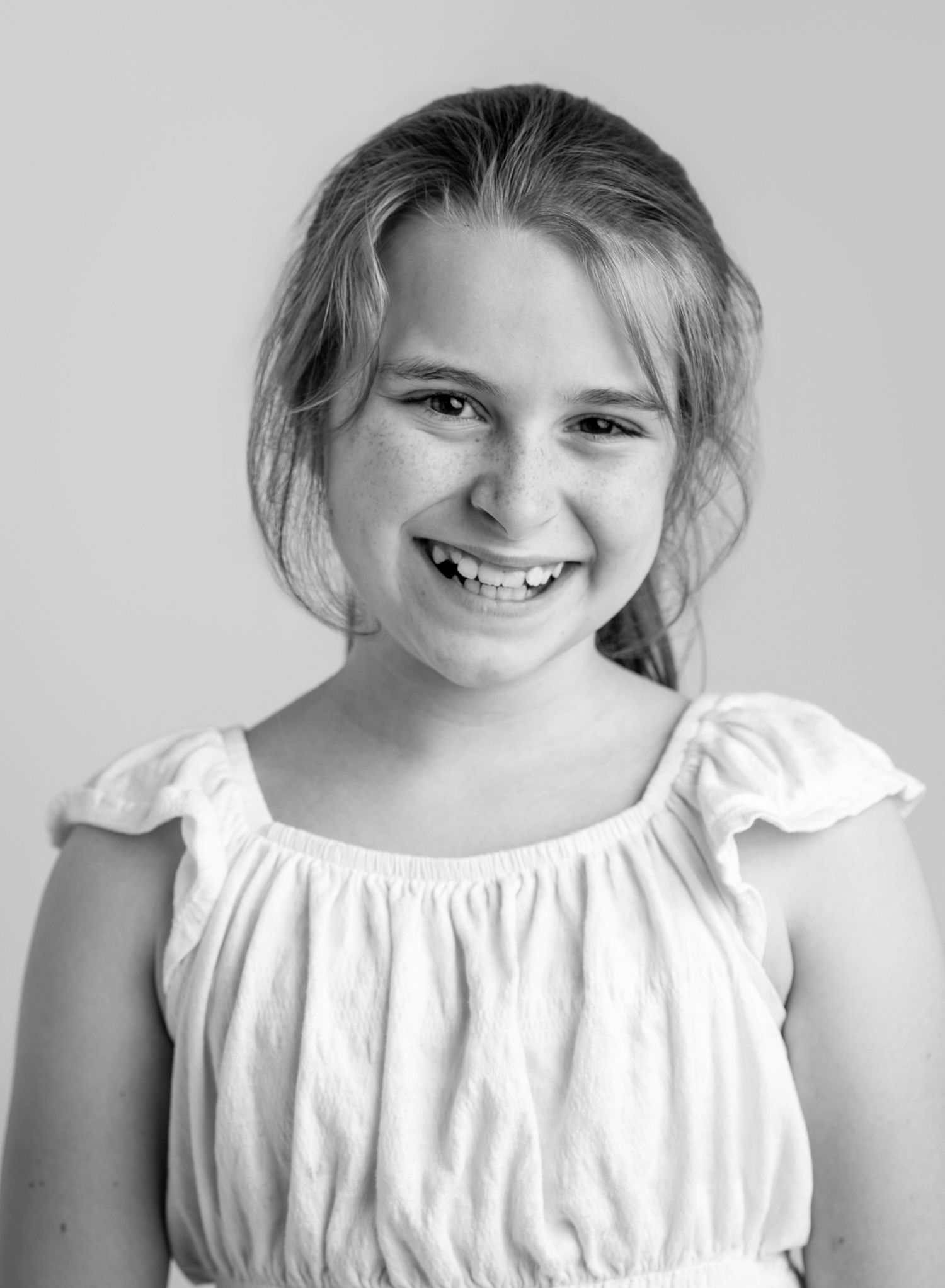 Black and white portrait of a smiling young girl with blonde hair wearing a white ruffled dress.