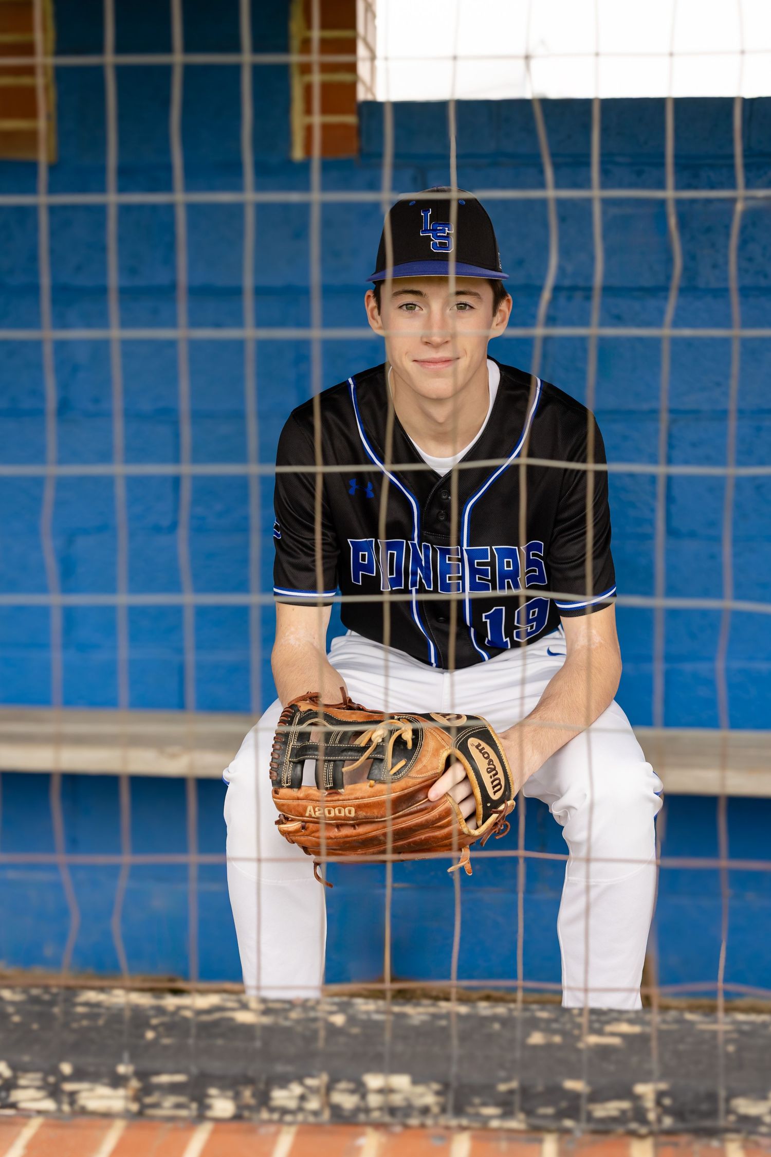 High school senior portrait of senior boy in baseball uniform, sitting in dugout with glove | sports high school senior portraits