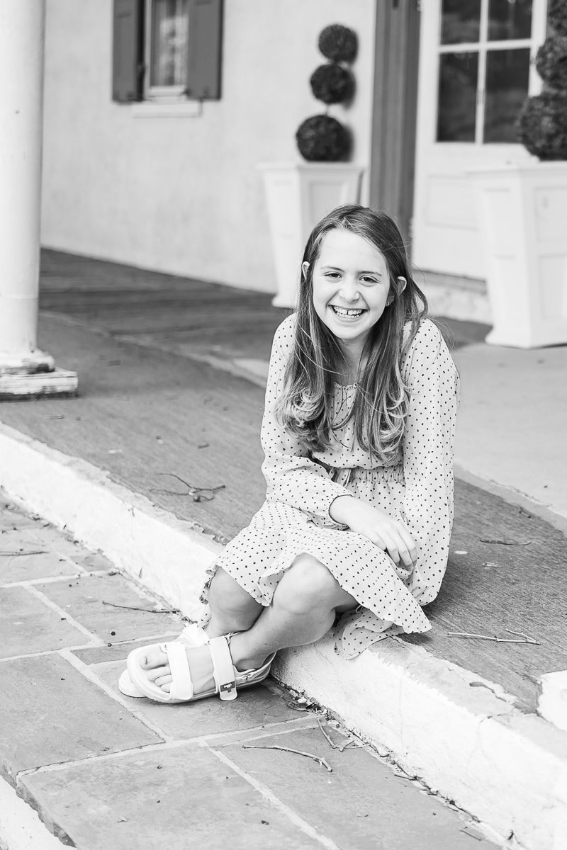 A family milestone session in Gap, PA at White Chimneys Estate. A black and white portrait of a beautiful teen girl sitting on stone steps.