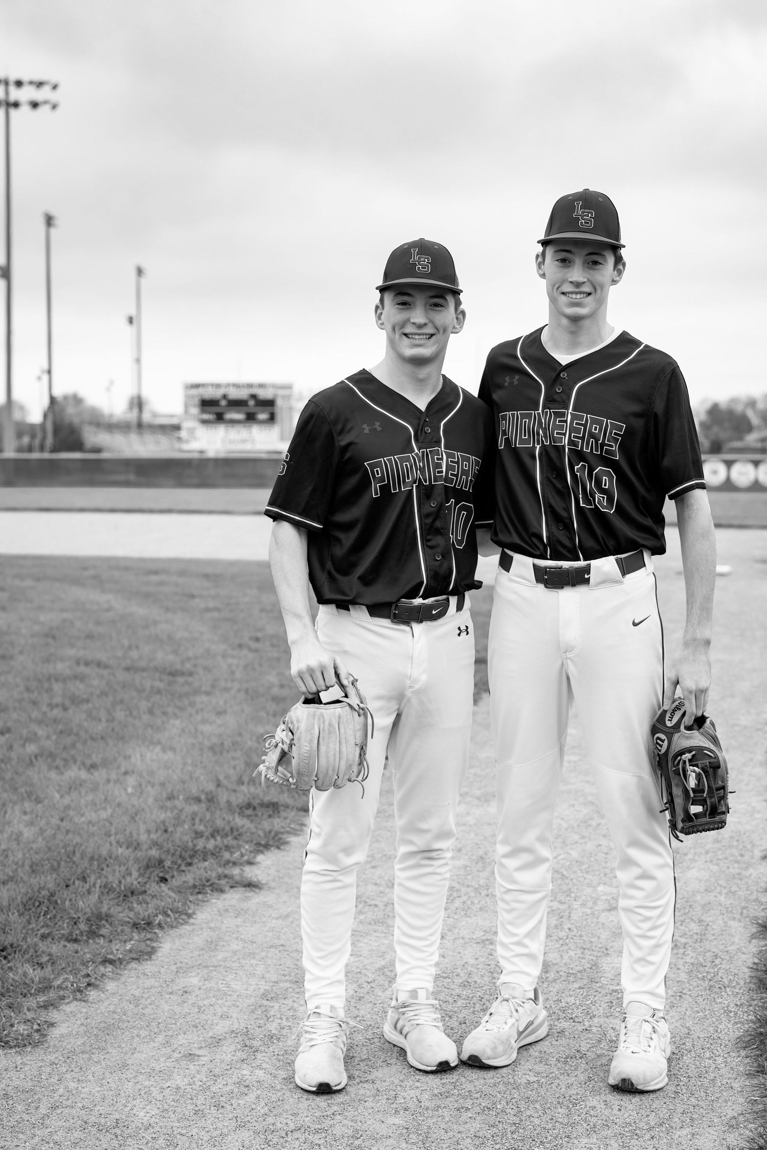 Black and white photo of two baseball players in uniforms standing together on a baseball field | High school sports senior portraits