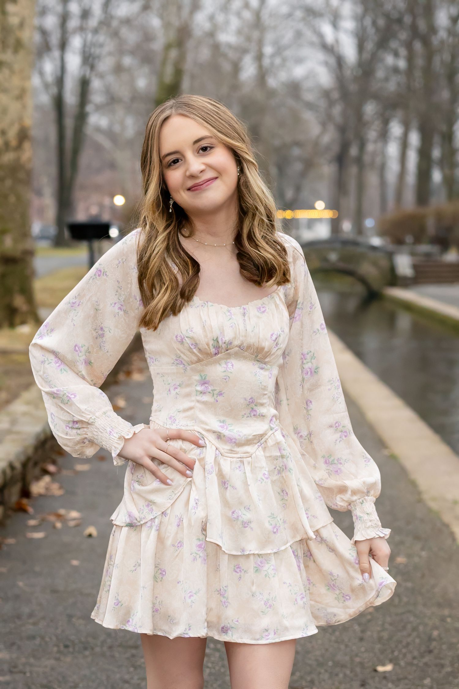 A beautiful high school girl in a floral pink and cream ruffle dress poses outdoors on a rainy autumn day.
