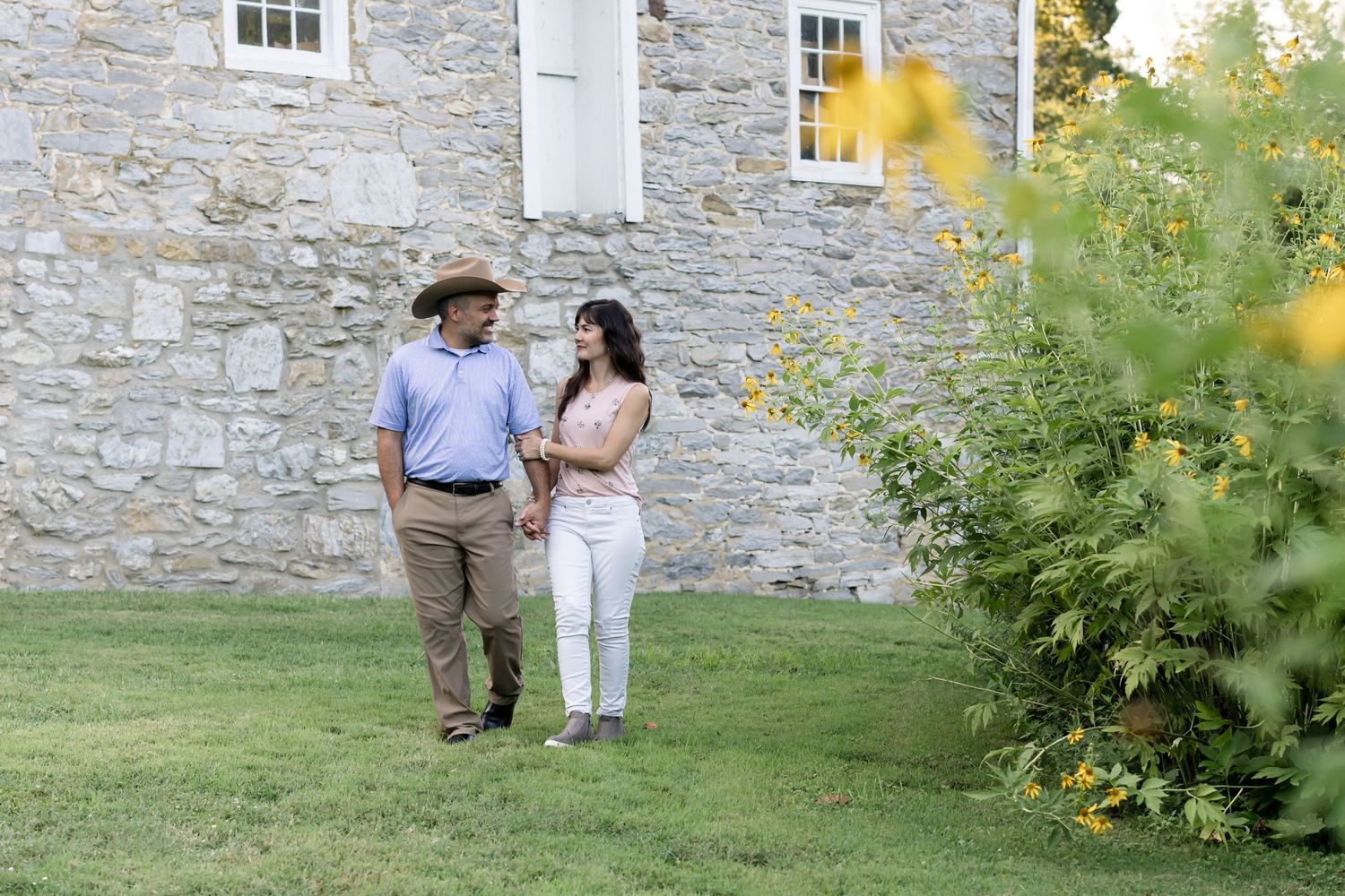 A couple walks together along a rustic stone wall on a sunny summer afternoon.