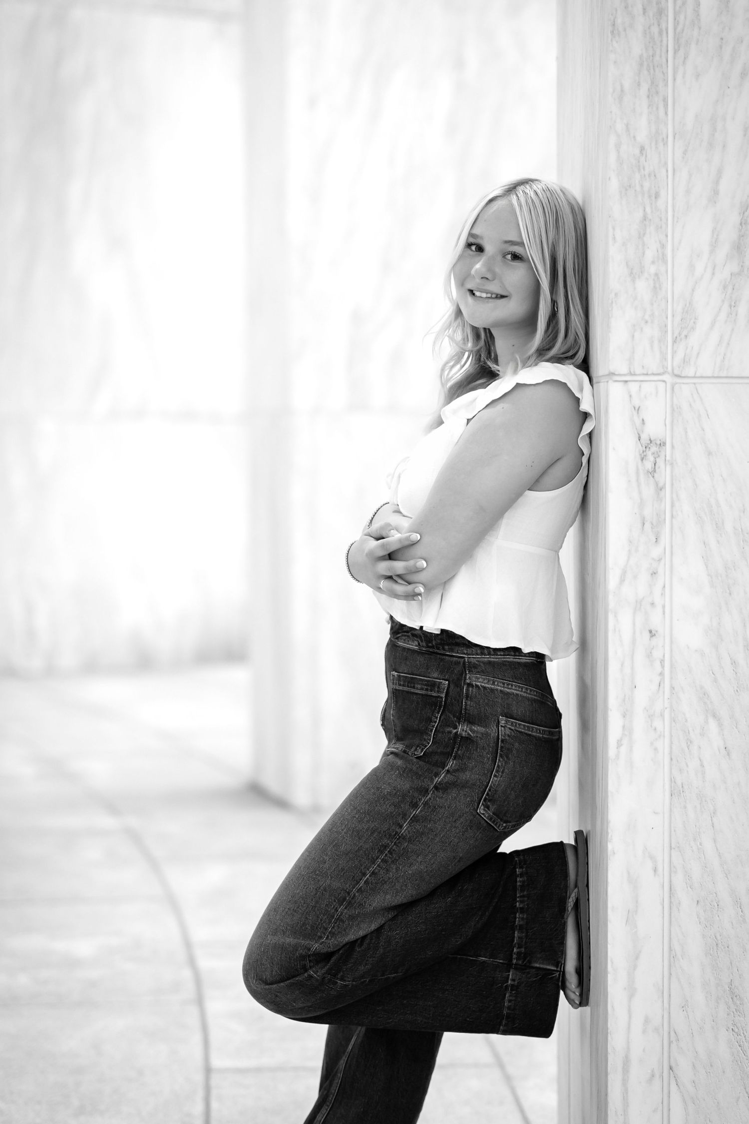 A black and white photo series showing a high school senior girl in casual attire posing against white columns in different positions.