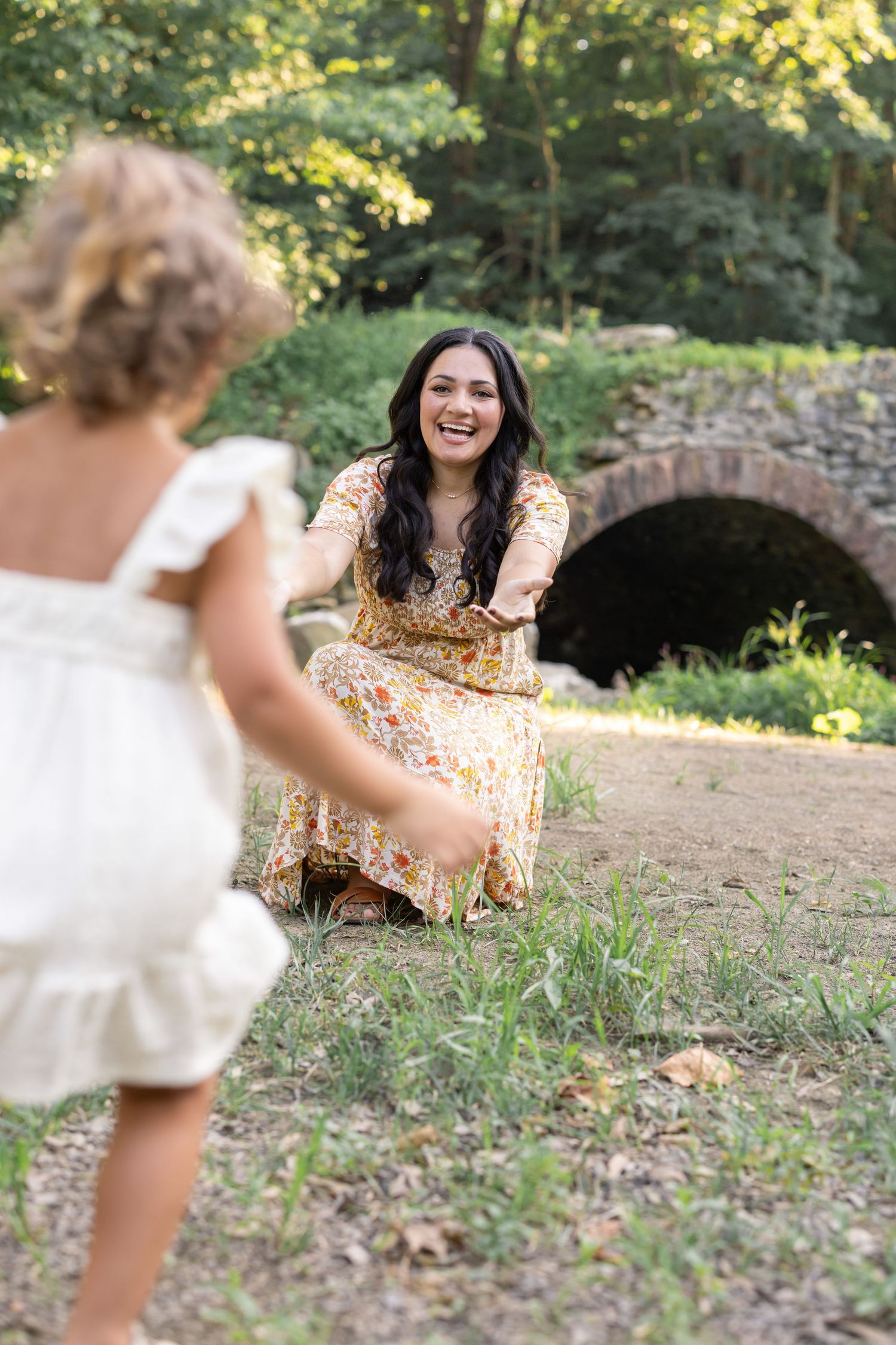 Two people share a joyful moment outdoors near a stone bridge, by Lancaster, PA luxury family photographer, Megan Mariah Photography.