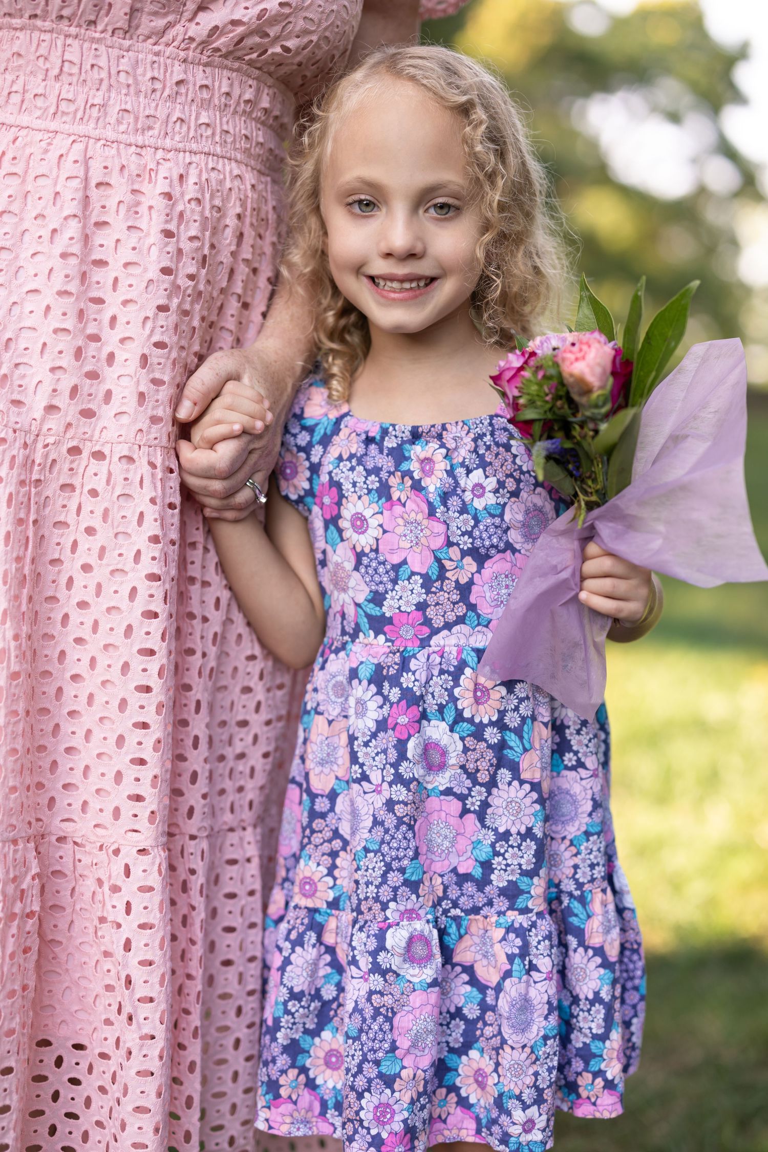 A young girl clutches her mother with one hand, and holds tight to a vibrant bouquet of florals with the other.
