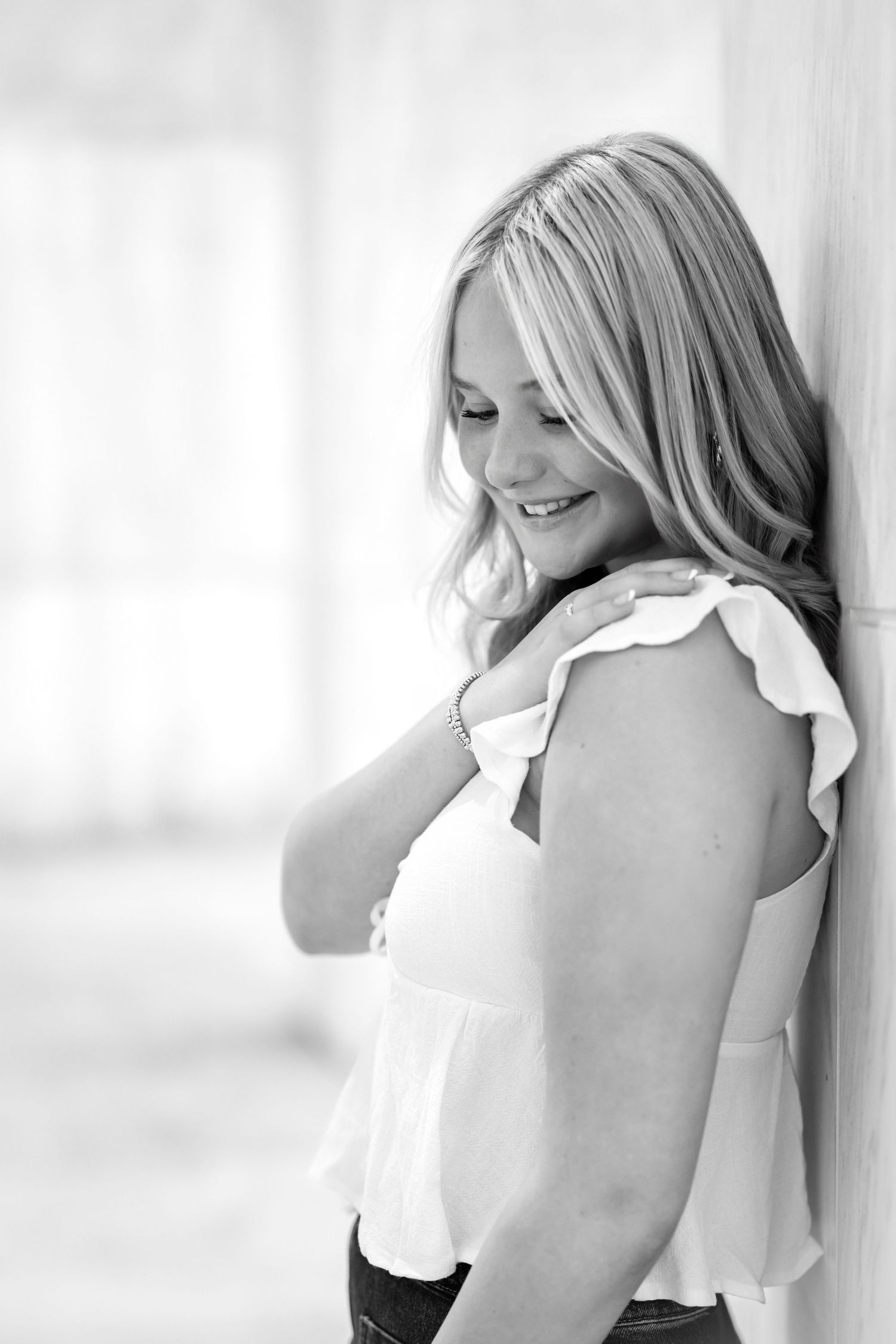 A black and white artistic portrait showing a high school senior girl in a white top against a light background.
