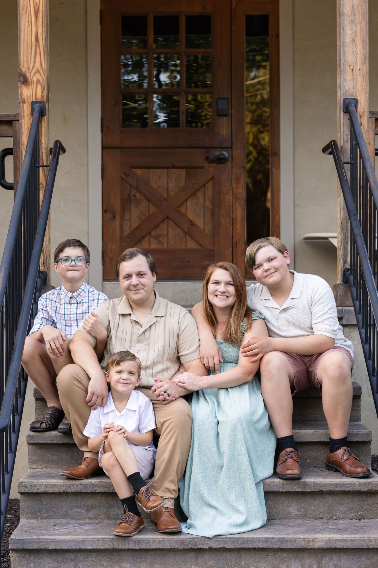 Family of five posing on front porch steps of a home, smiling together for a portrait photo.