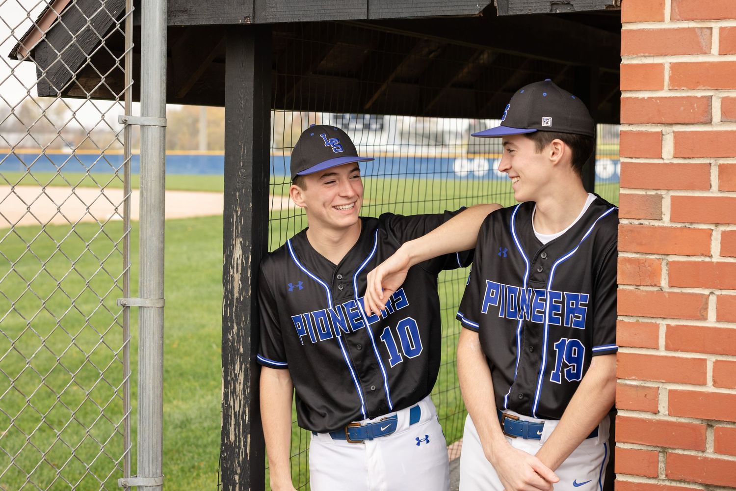 Senior friends session by Megan Mariah Photography | two brothers in baseball uniform chatting by the dugout in candid moment
