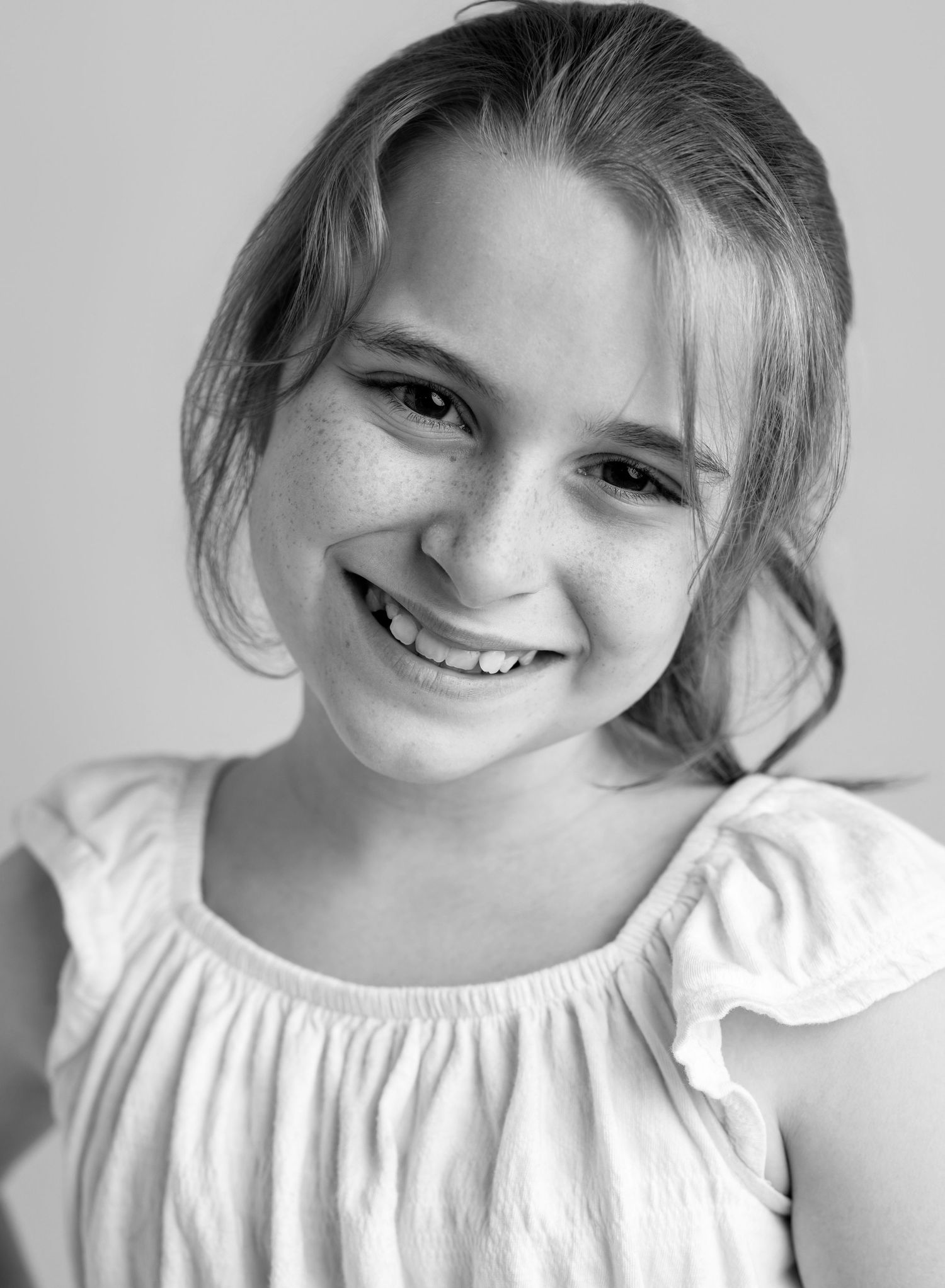 Black and white portrait of a smiling young girl with freckles wearing a white ruffled top.