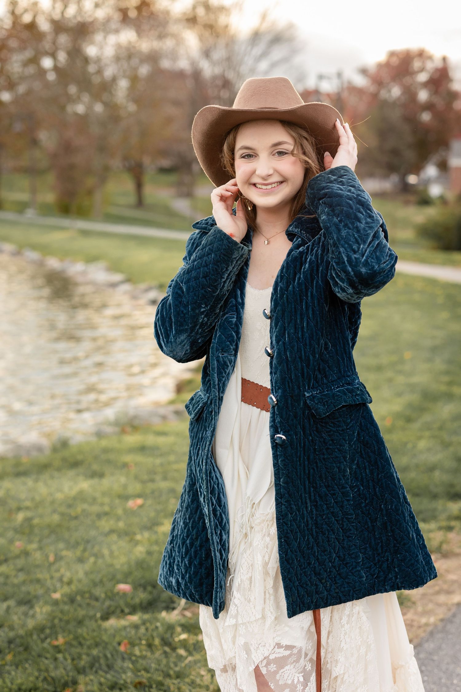 Fall senior portrait of a girl in a cowgirl hat and white flowing dress in a natural outdoor setting.