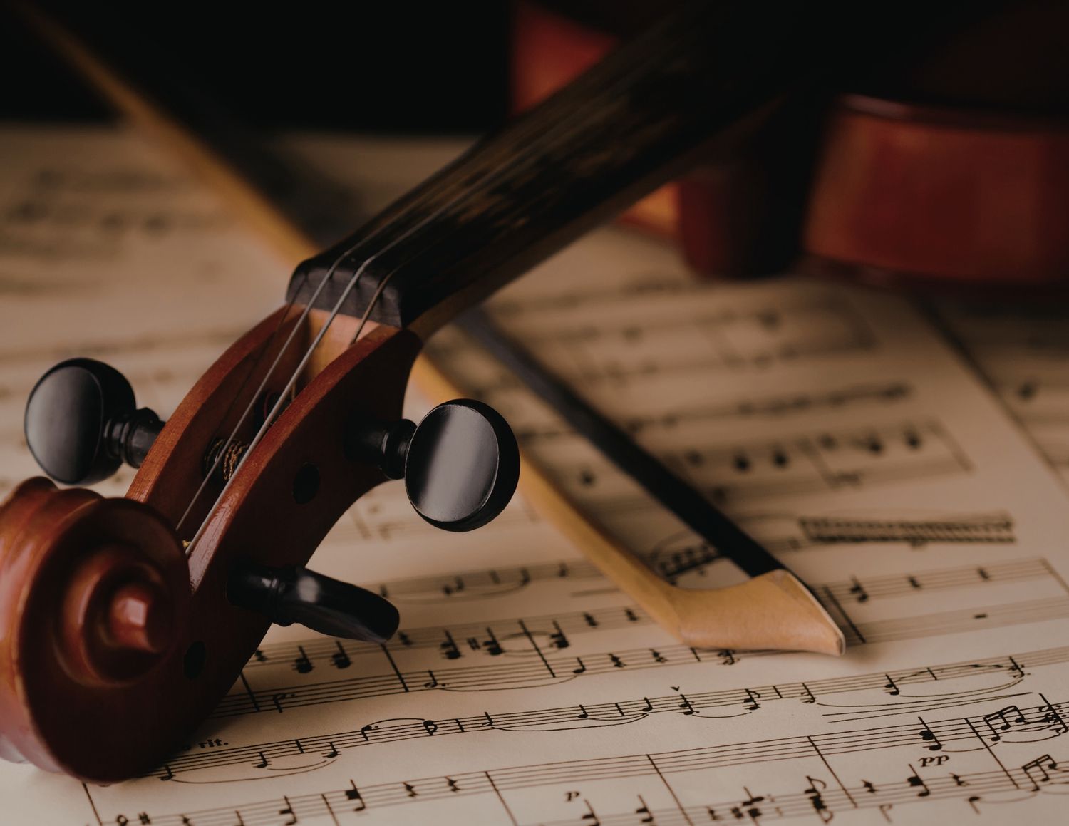 Close-up view of a violin scroll resting on sheet music with musical notes visible in the background.