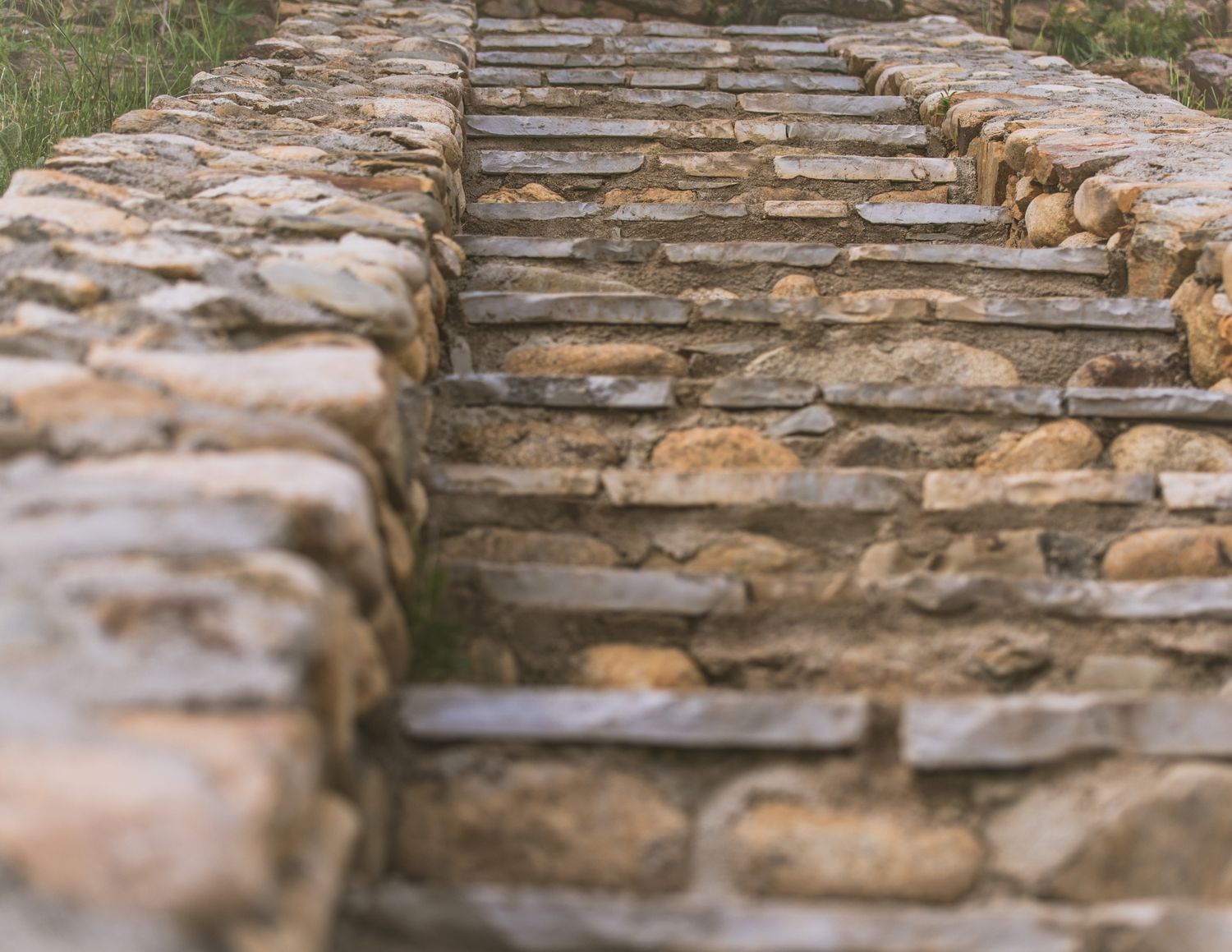 Rustic stone staircase with flat rock steps flanked by dry-stacked stone walls, leading upward in a natural outdoor setting.