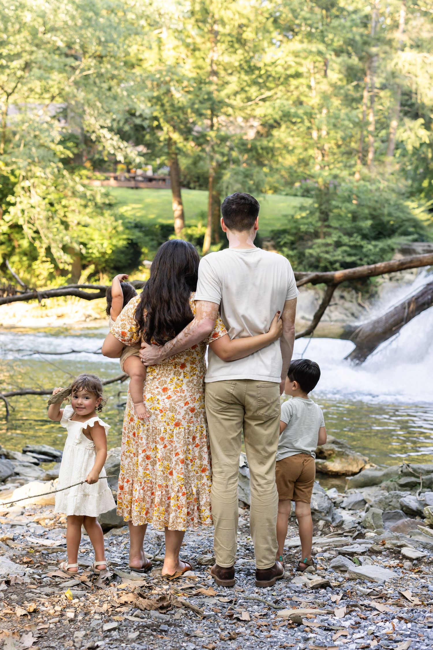 Family of four standing by a waterfall in a lush green forest, viewed from behind.