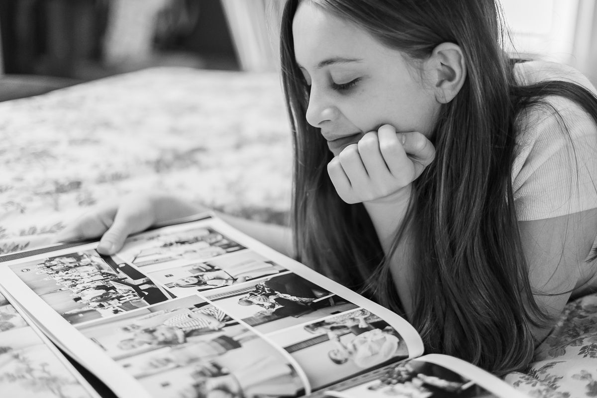 A black and white image of a teen girl looking at an heirloom album, by Megan Mariah Photography in Lancaster, PA.