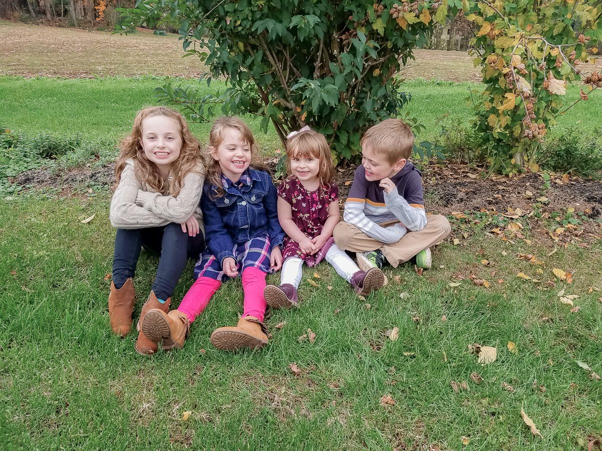 Children lying on autumn grass wearing colorful clothing play together in a lawn during fall season.