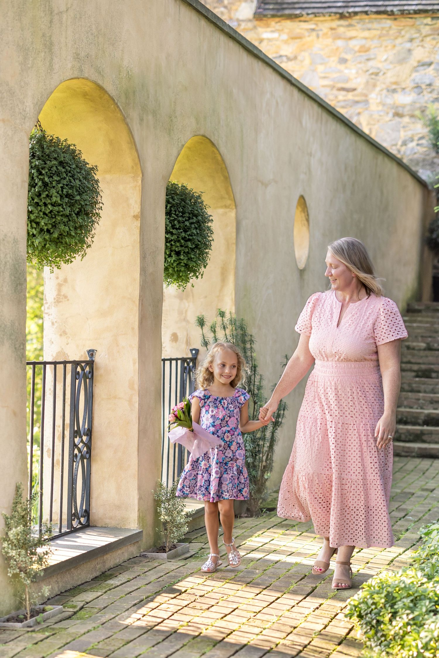 Mother and young daughter walk hand and hand past architectural feature wall during a mother-daughter photo session in Lancaster, PA.