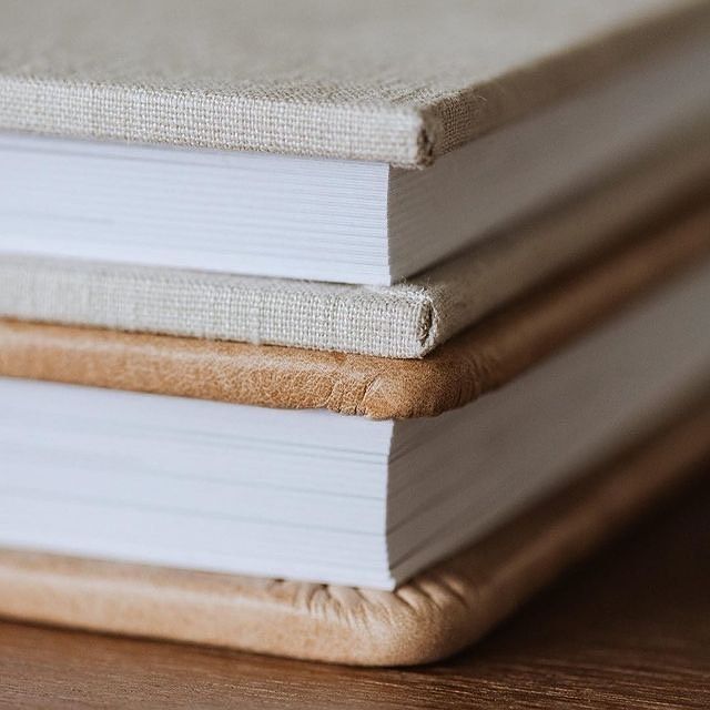 A detail image of a beige linen album and a light brown leather album sold by Megan Mariah Photography for senior and family portraits.