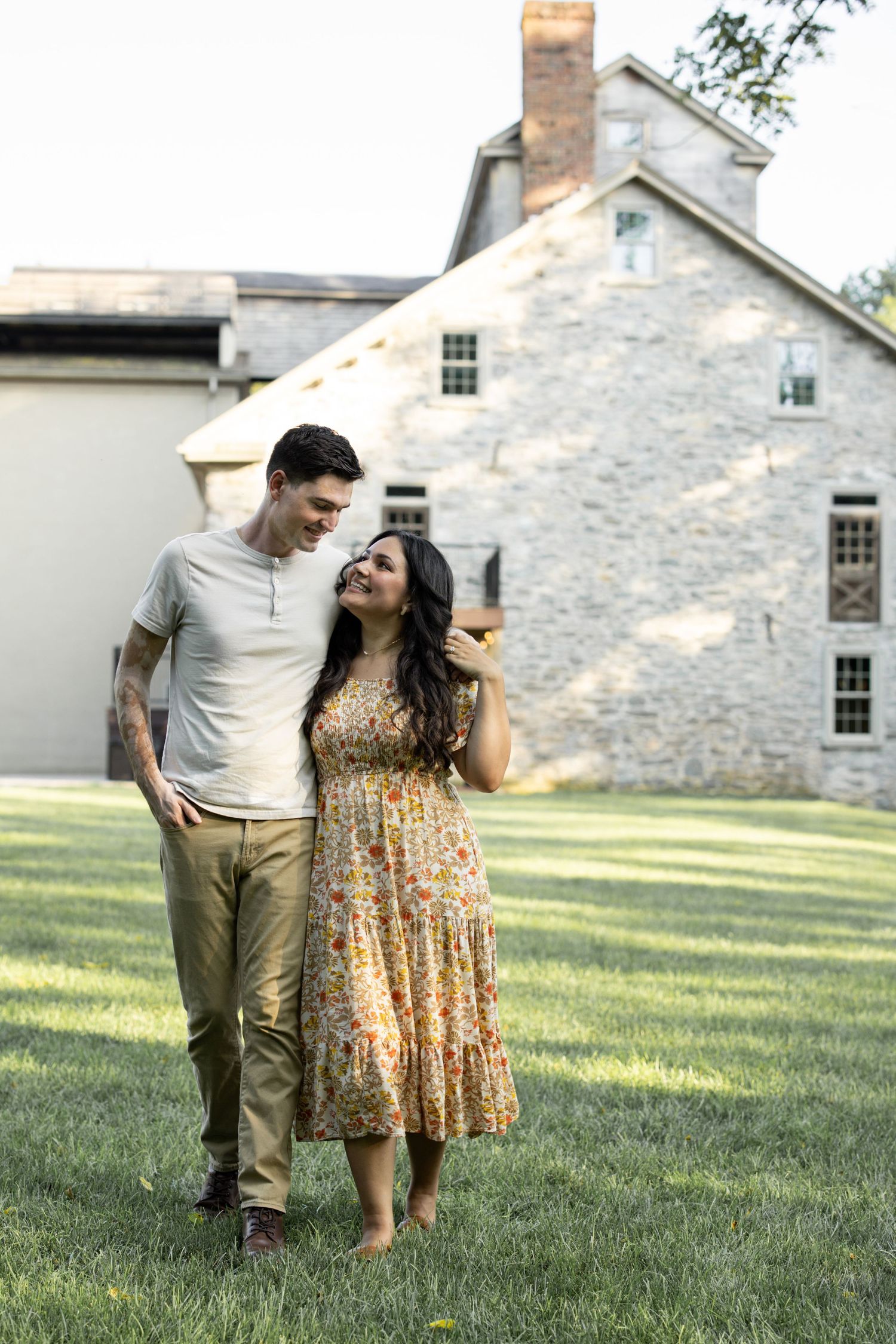 A romantic outdoor scene with a couple walking on grass in front of a rustic stone building on a sunny day in Lancaster, PA.