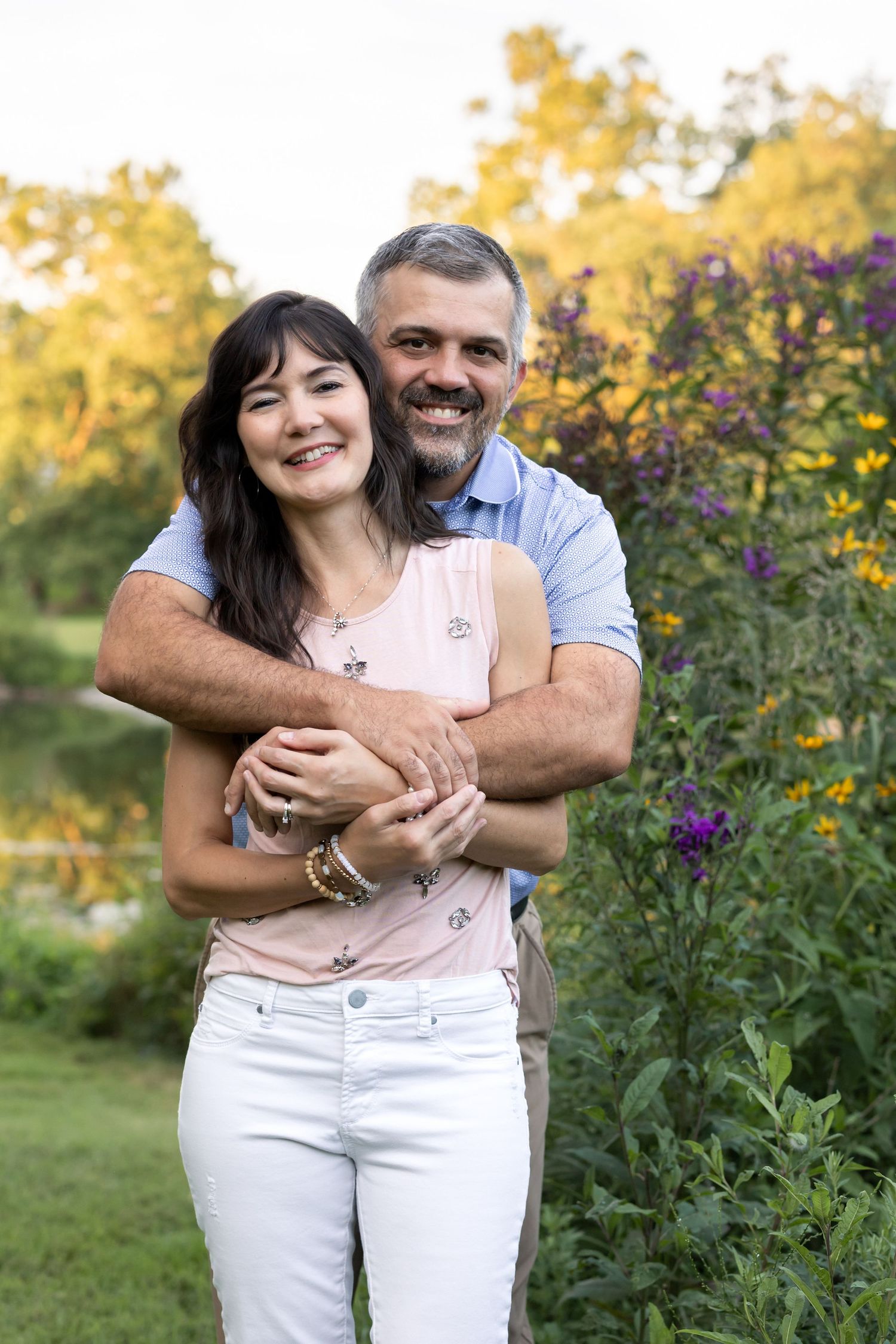A beautiful couple embracing surrounded by lush greenery and with pops of color from seasonal blooms at Grings Mill in Reading, PA.