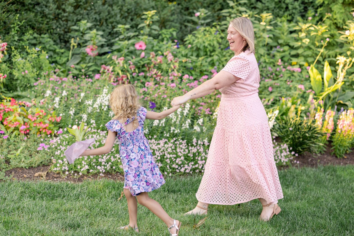 A young girl takes her mother's hand as they stroll through a beautiful, lush garden, image by a Lancaster, PA family photographer.