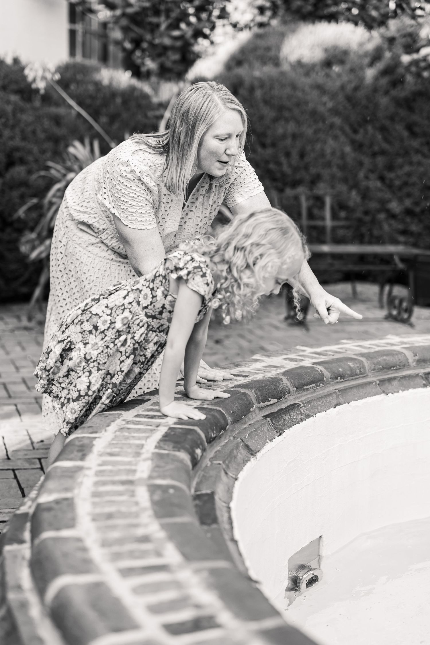 A black and white image shows a mother and daughter viewing a fountain in a garden during a mother-child photo session in Lancaster, PA.