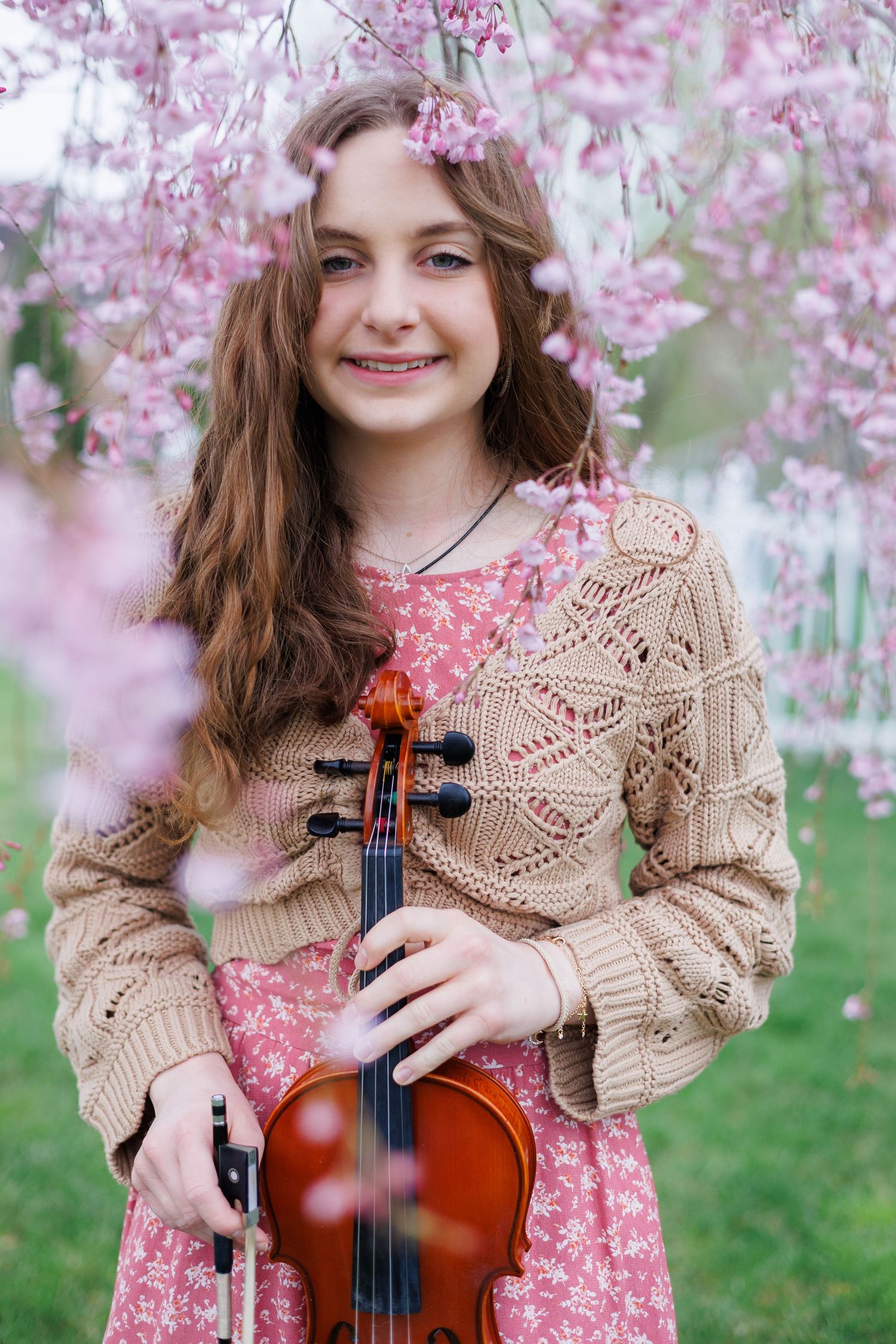 A high school senior musician poses with a violin under blooming pink cherry blossoms in spring.