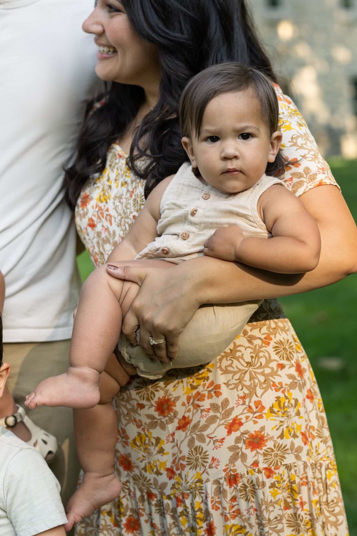 Woman in floral dress holds baby wearing beige outfit while standing outdoors during golden hour in Lancaster, PA.