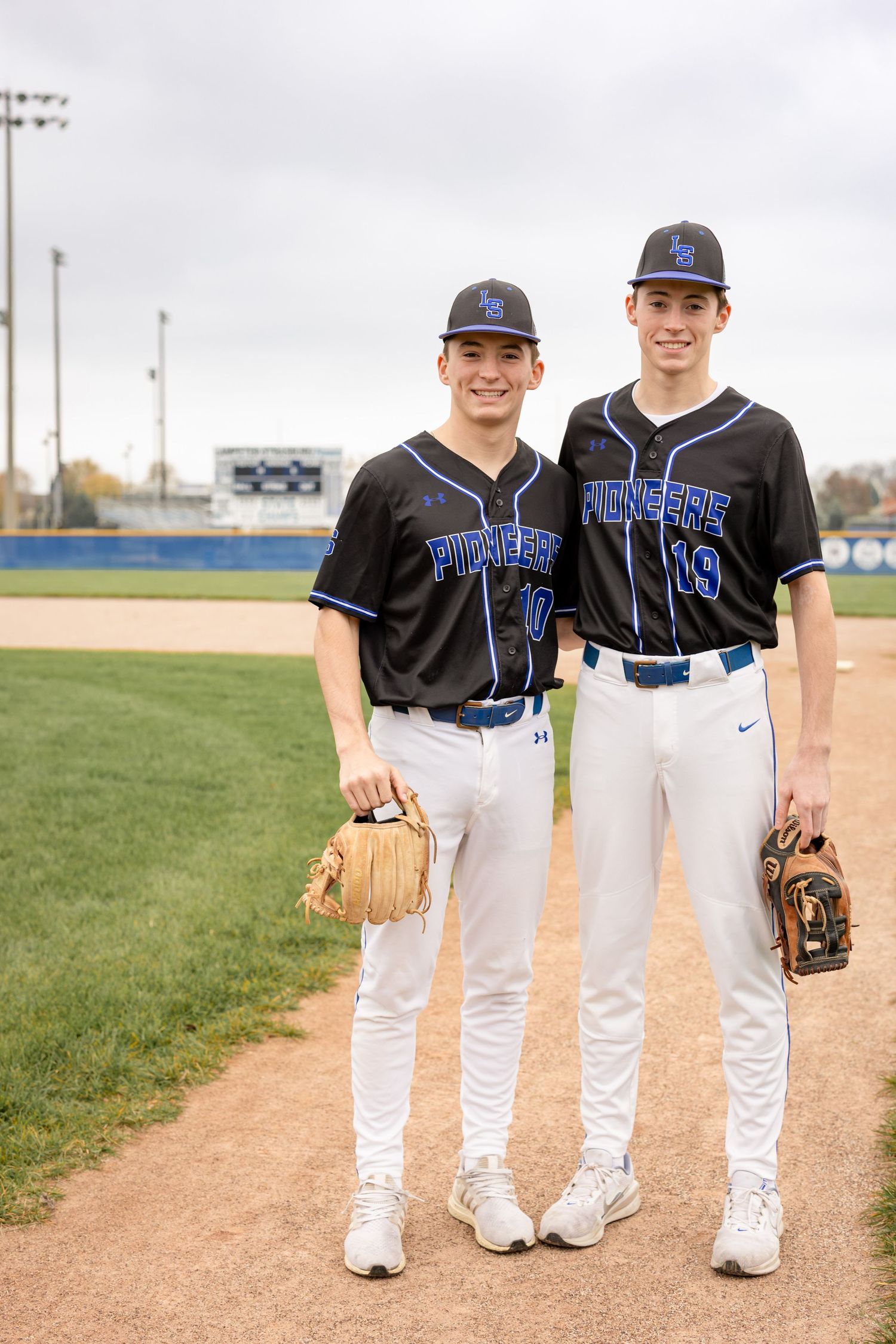 Two high school senior brothers posed in uniform on their home baseball field during their photo session