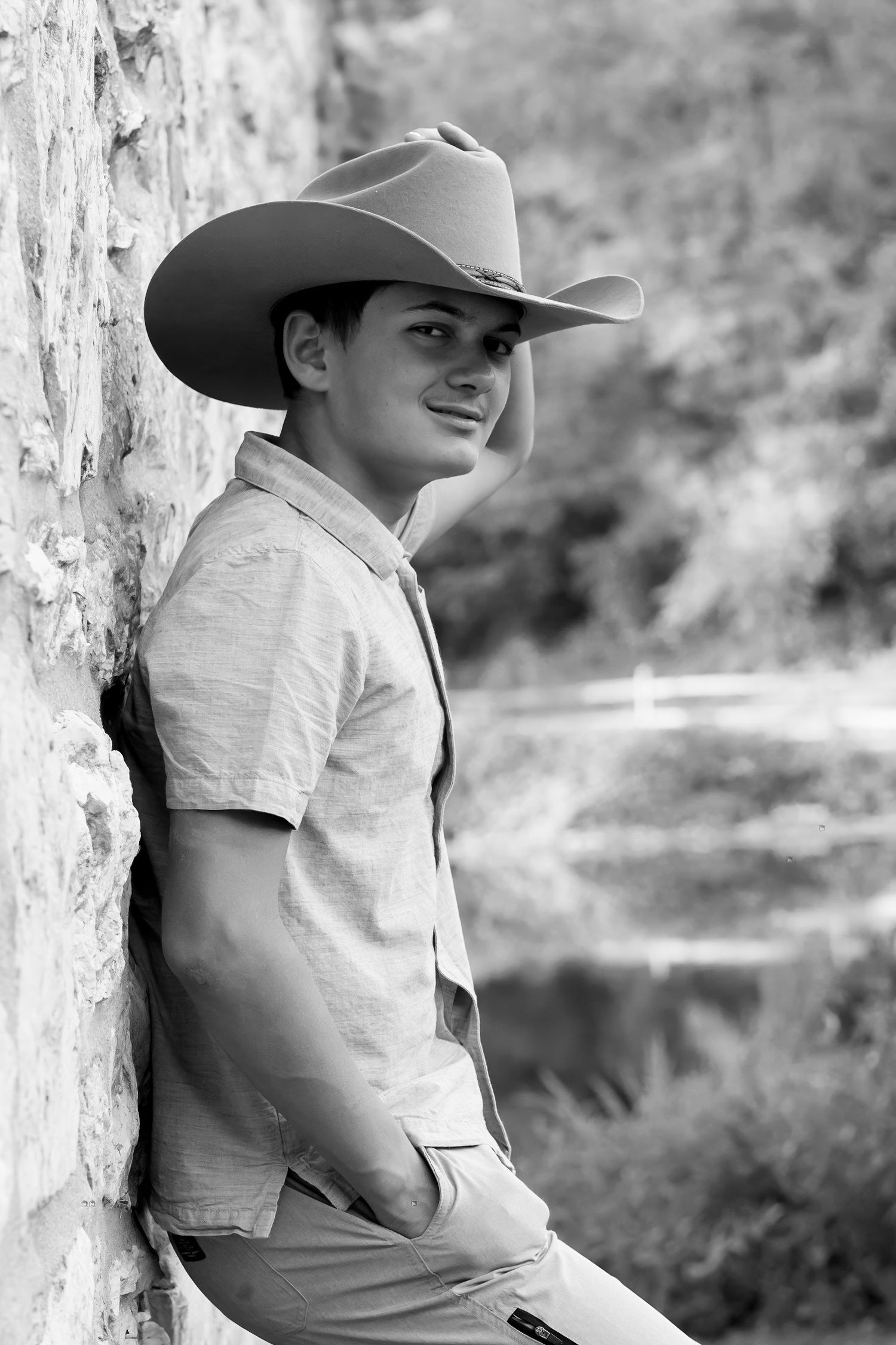 A black and white senior photo shows a young man leaning against a stone wall in a cowboy hat in Lancaster, PA.