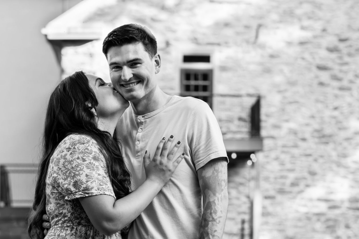 Black and white romantic portrait of couple embracing by stone building.