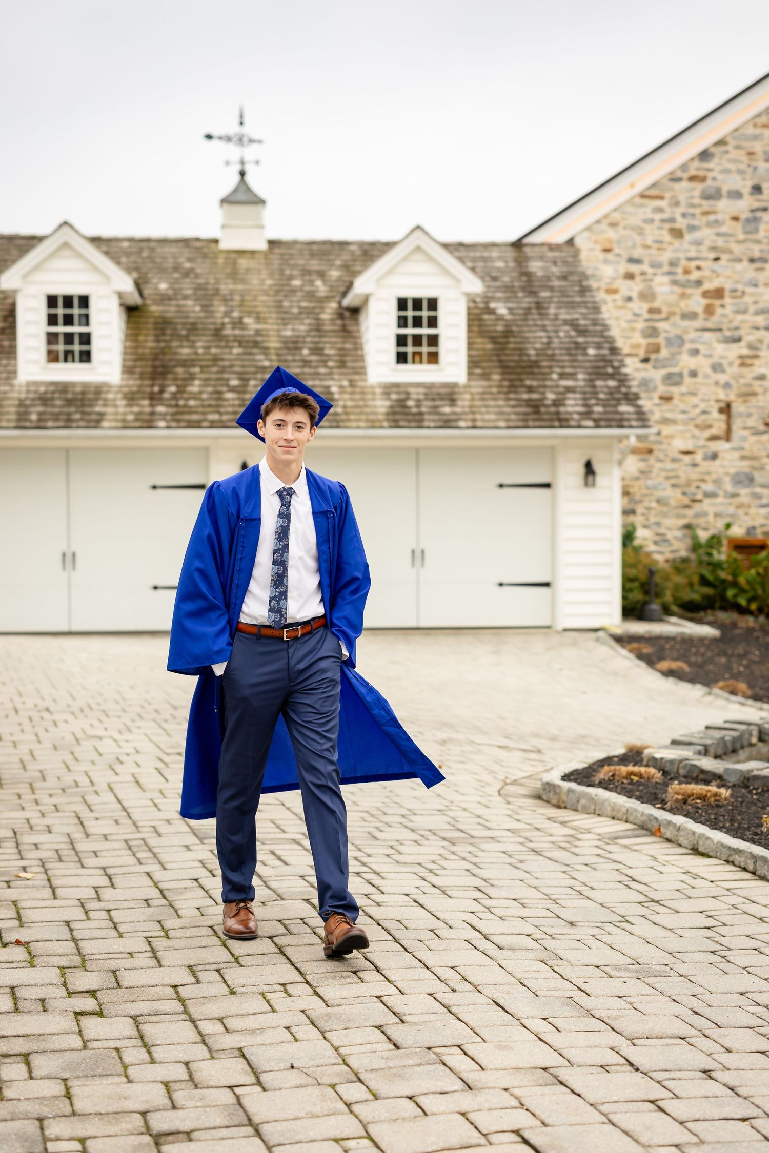 High school senior boy walking in blue cap and gown during luxury senior portrait session
