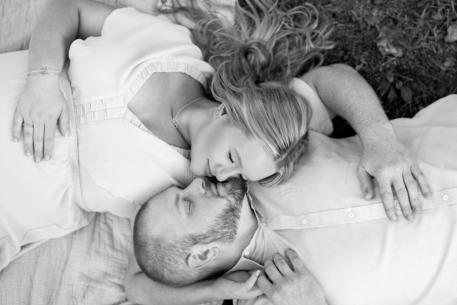 Black and white photo of a couple lying down together, sharing a tender romantic moment outdoors.